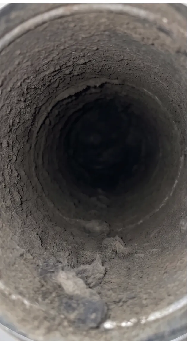 Inside a round dryer vent pipe caked with dust and lint before cleaning
