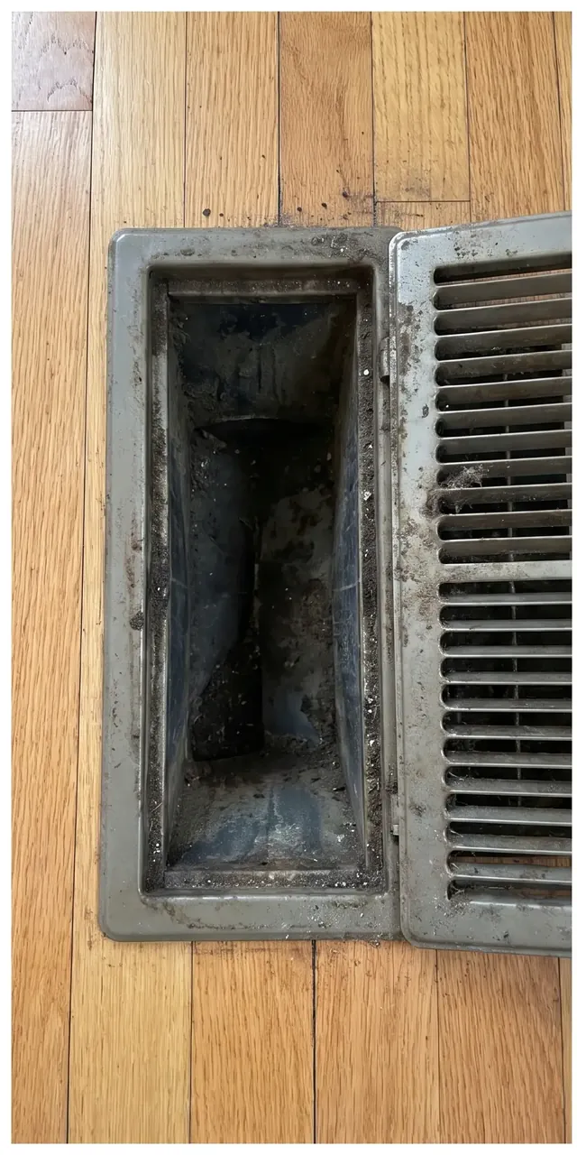 Floor vent opening and register grille coated in dust and grime before cleaning